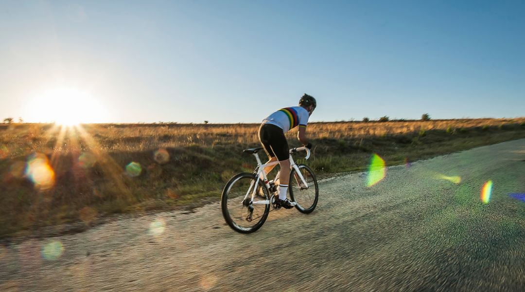 A gravel cyclist sprints along a dirt road at sunset.
