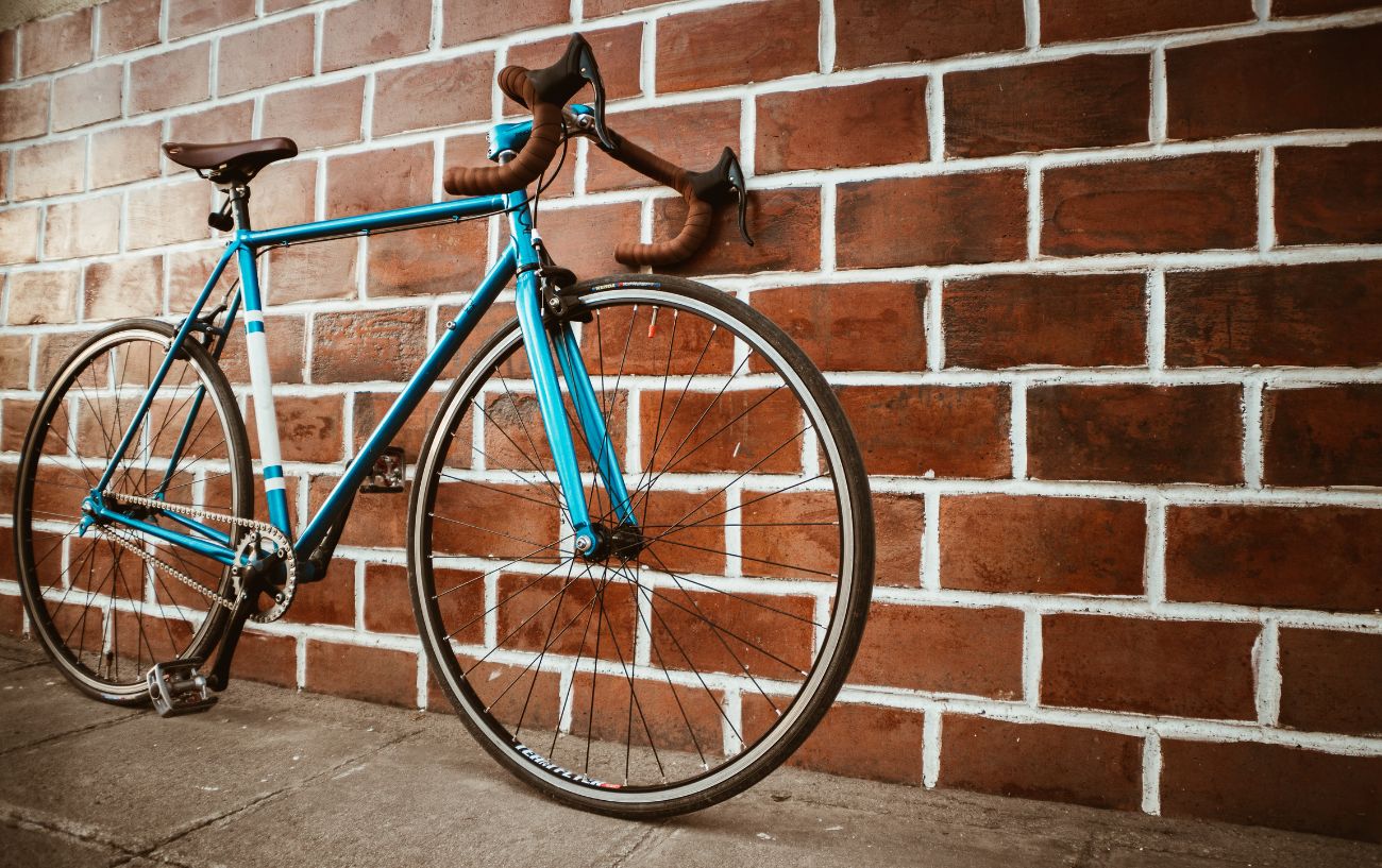 A turquoise road bike with 700c wheels and tires leans against a brick wall.