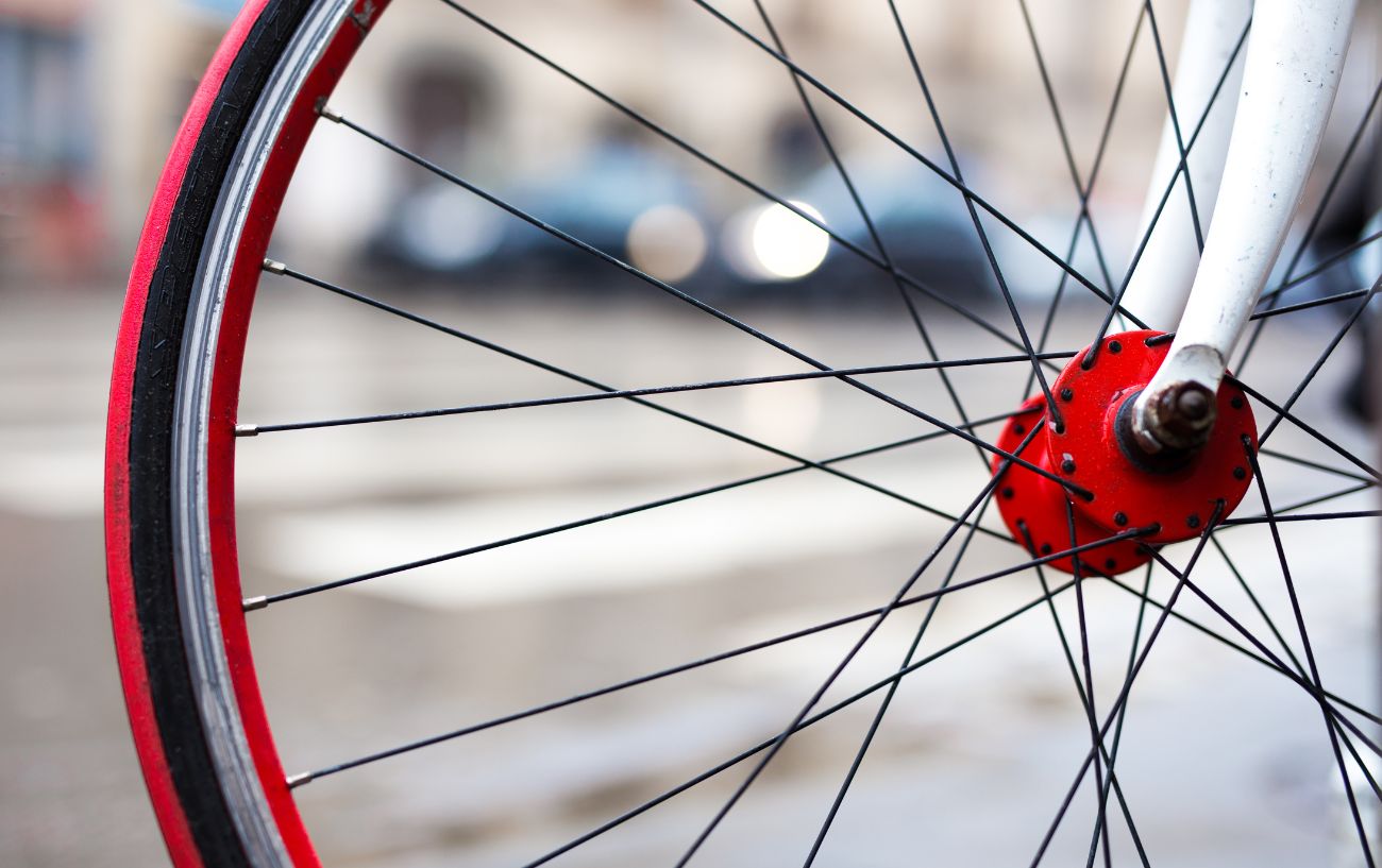 A white road bike with 700c wheels, fitted with red hubs, rims, and tires.