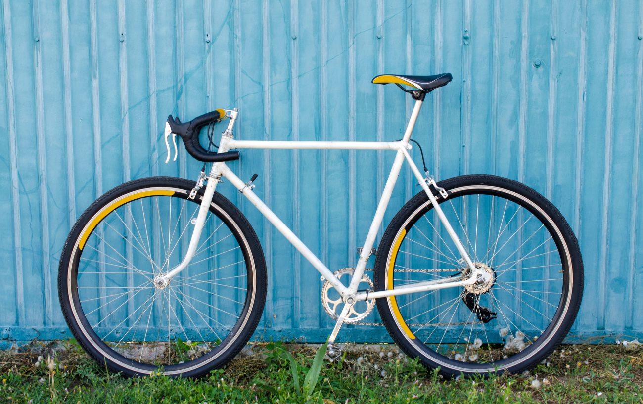 A white road bike with 700c wheels against a blue wall.