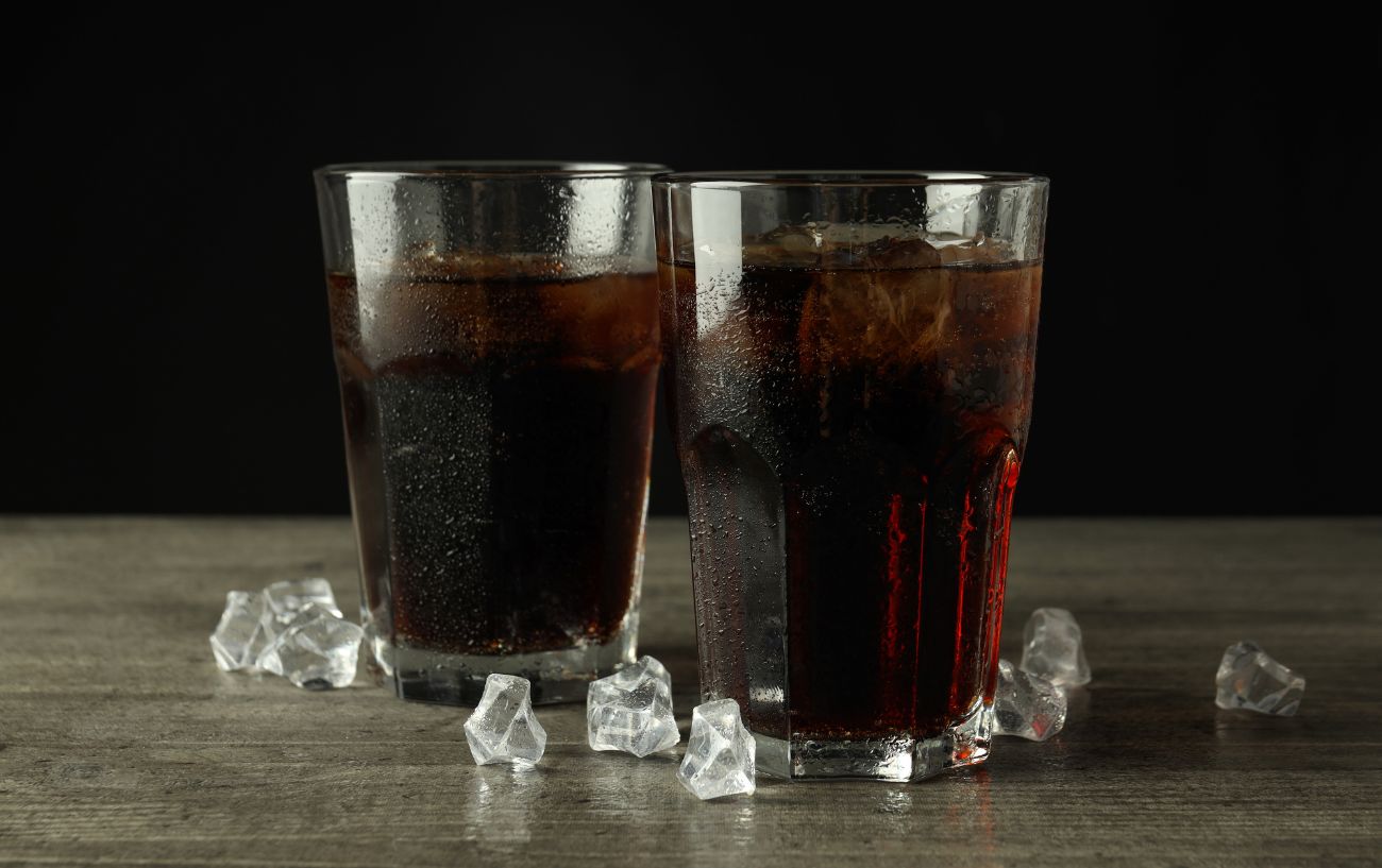 Two glasses of cola filled with ice against a flat background.