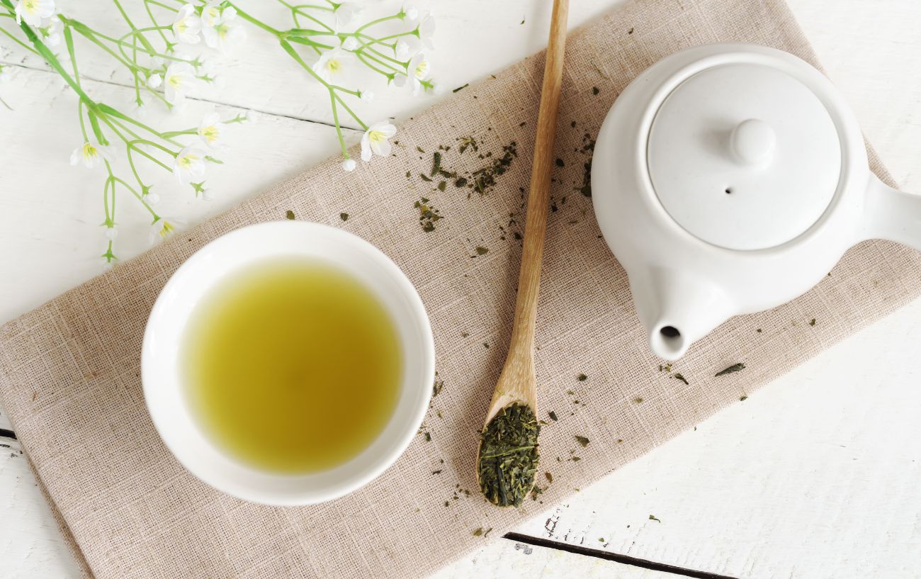 A pot of green tea on a beige tablecloth.