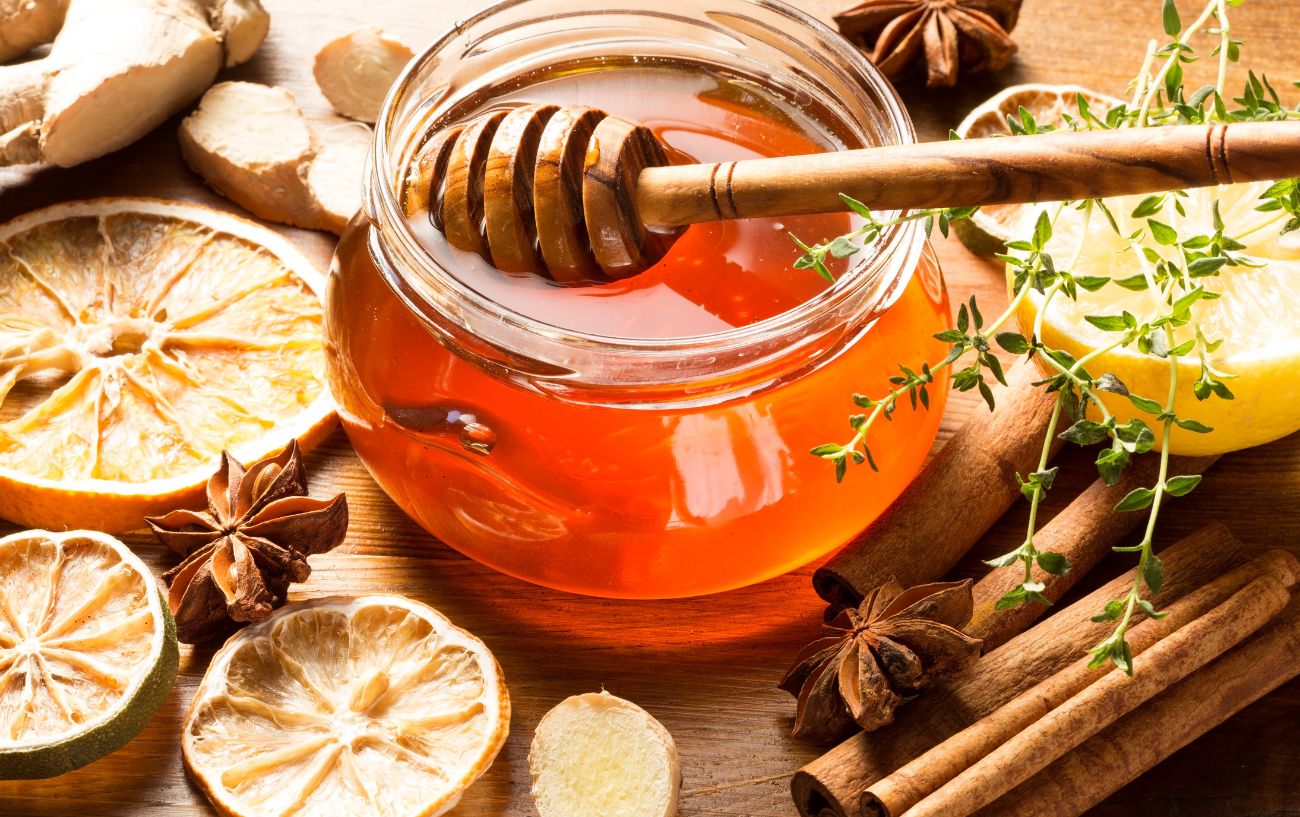A pot of honey surrounded by spices such as star anise and cloves.