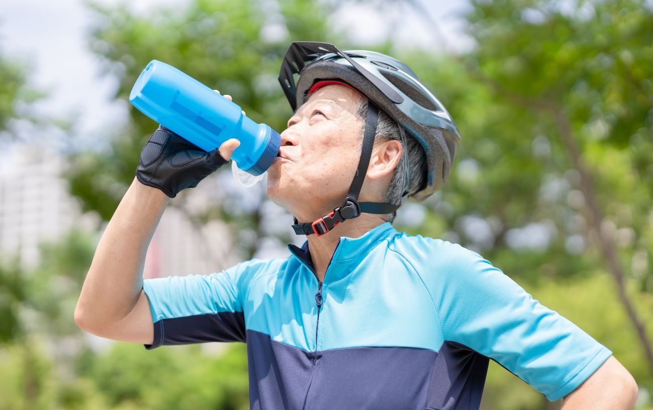 A cyclist in a blue jersey drinks an energy drink.