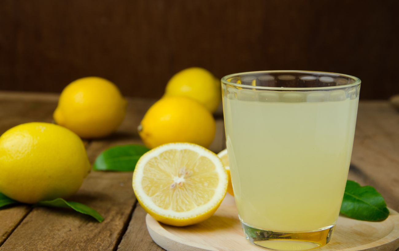 A cup of lemon juice surrounded by halved lemons.