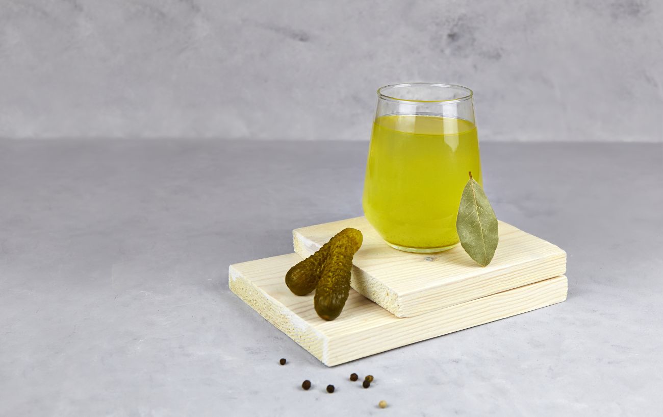 A glass of pickle juice sits on a chopping board.