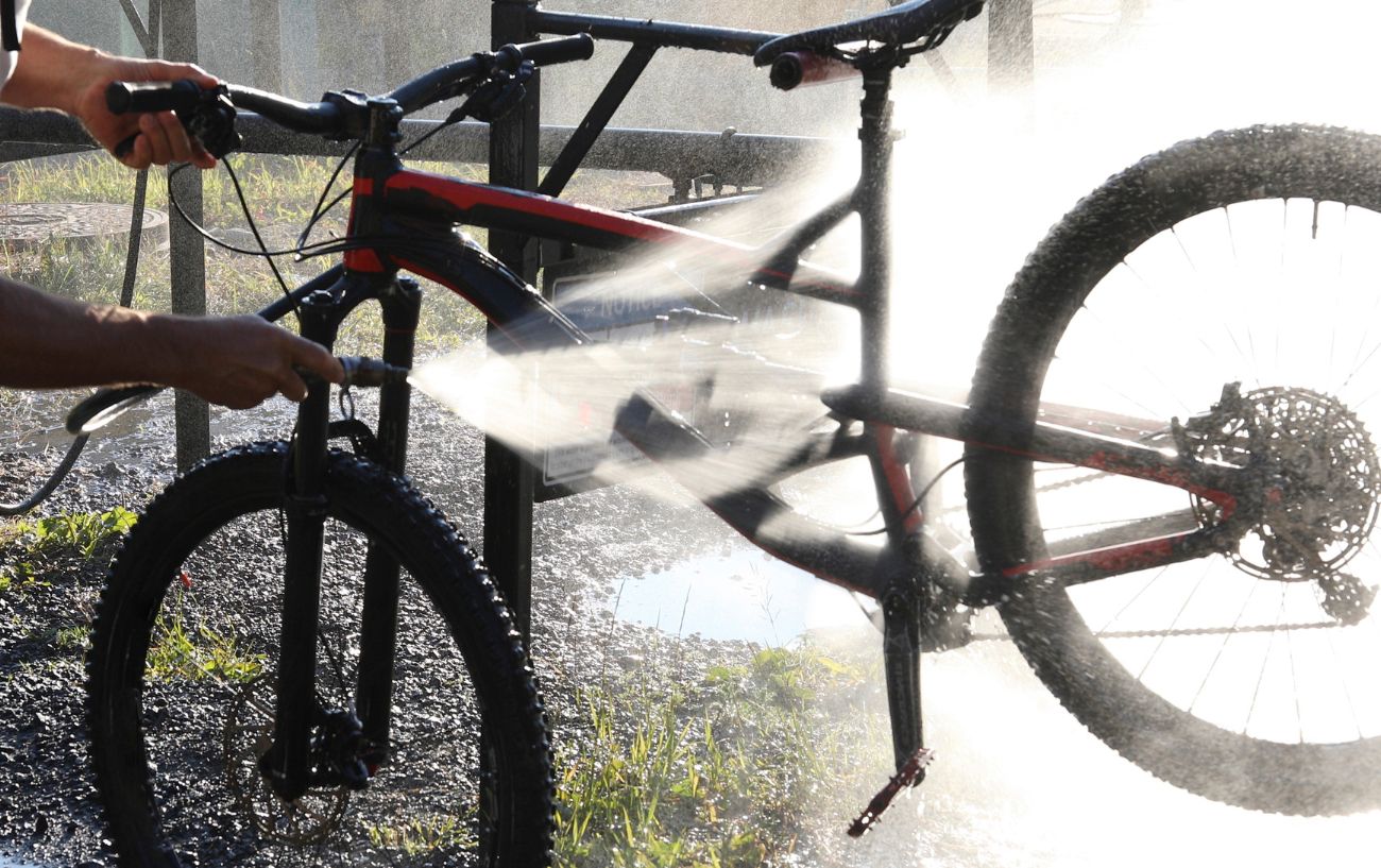 A cyclist cleans their black mountain bike with a power hose.