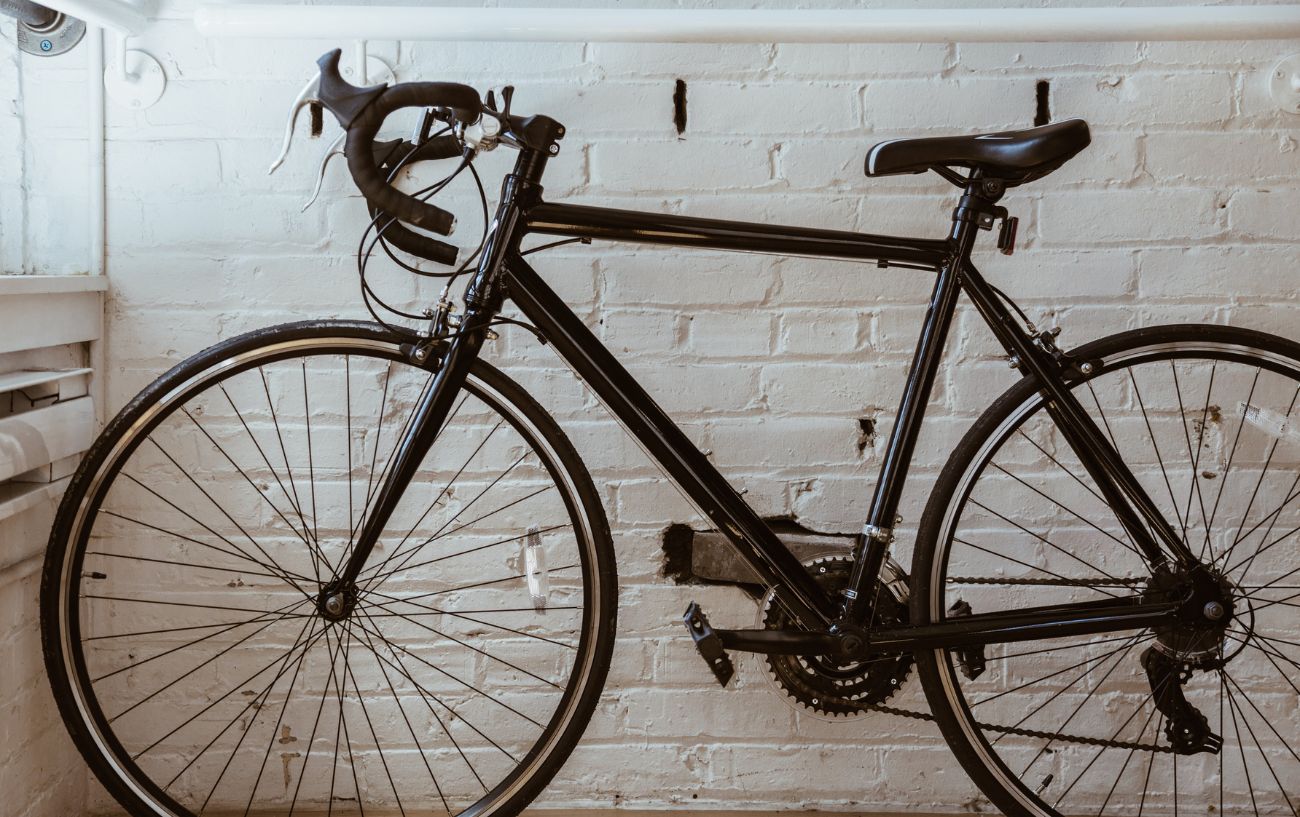 A black road bike leans against a whitewashed brick wall.