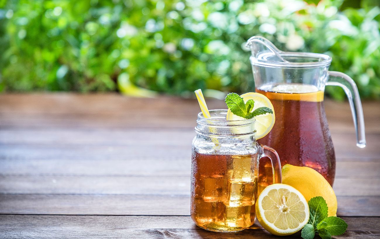 A jug of ice tea and a filled jar sit on a wooden bench.