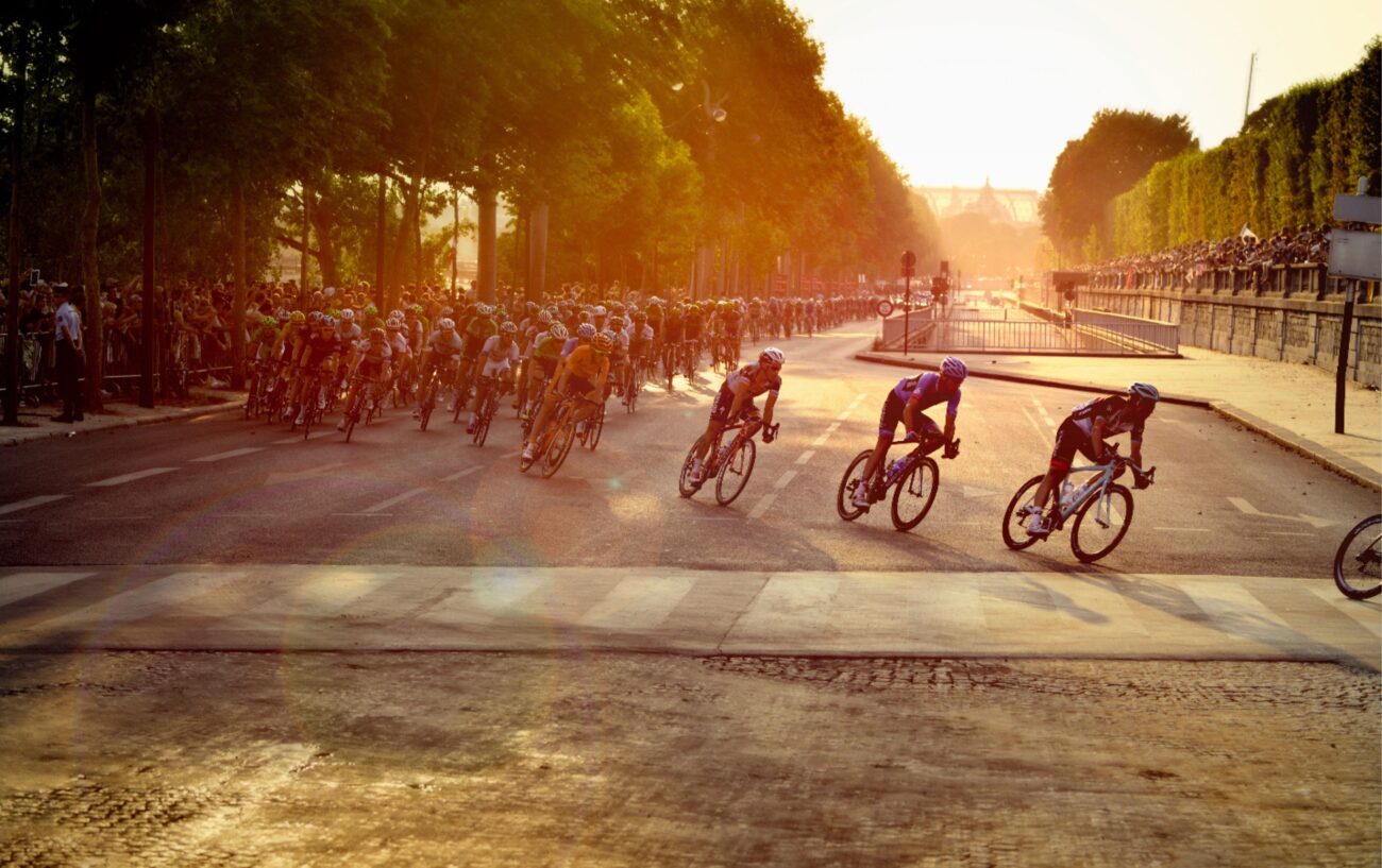 The Tour de France peloton races through Paris at sunset.
