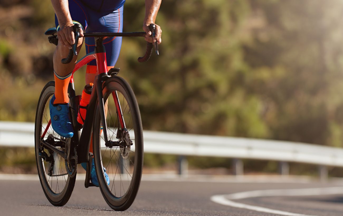 A cyclist climbs a steep hill on an orange road bike.