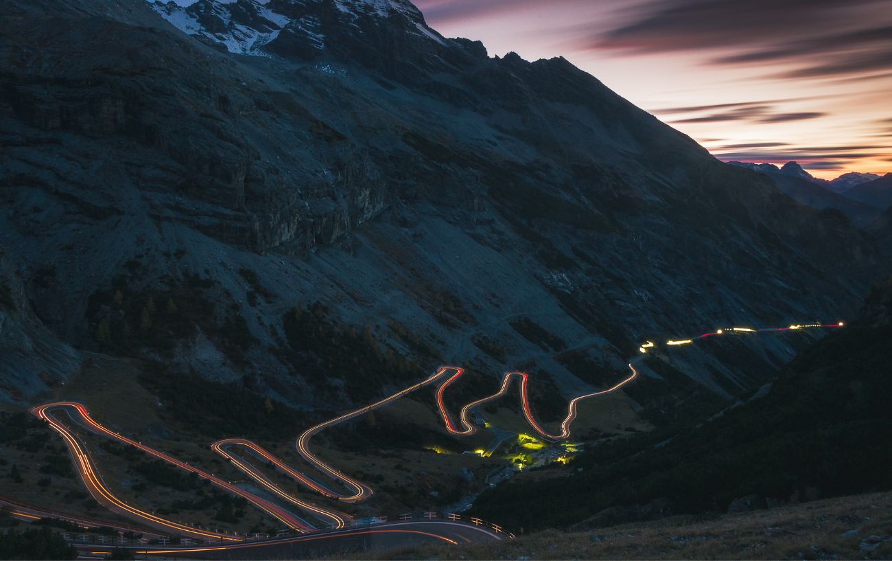 Headlights streak up the Passo dello Stelvio at dusk.