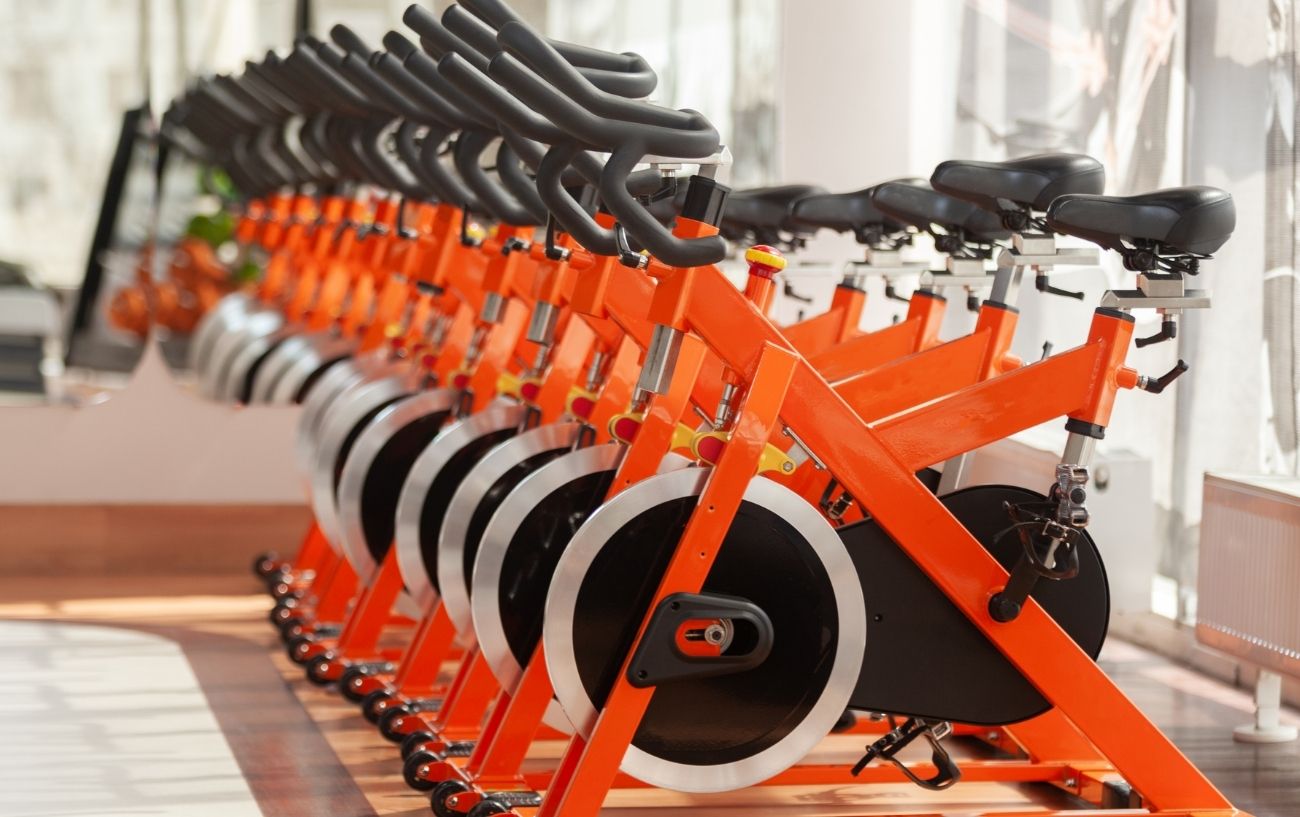 A row of orange spin bikes in a gym studio.