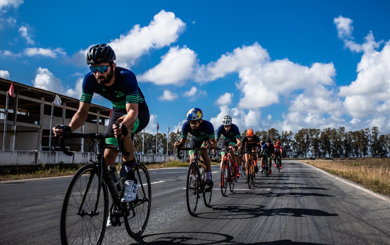 A group of cyclists with shaved legs ride around a race track.