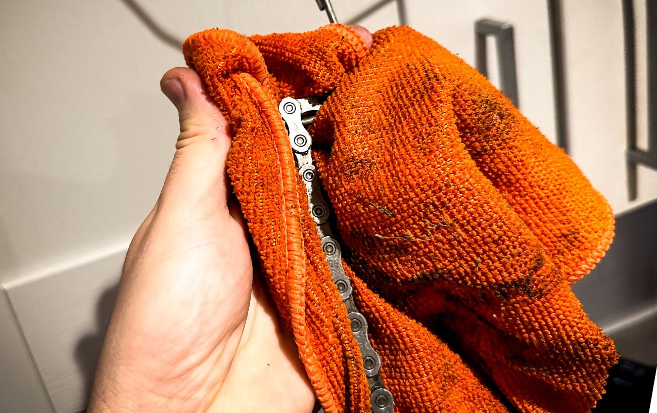 A waxed bike chain is cleaned with an orange rag.