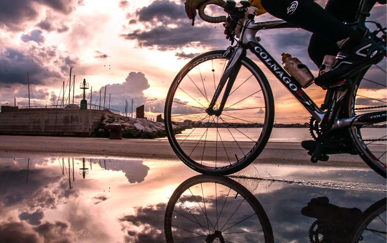 A cyclist rides a black Colnago through a port at sunset.