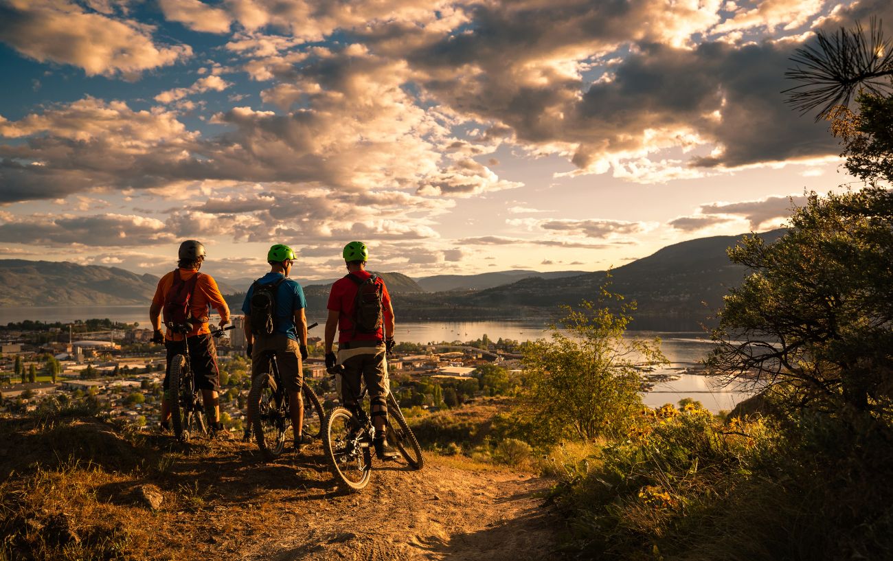 Three mountain bikers admire a sunset view across a river.