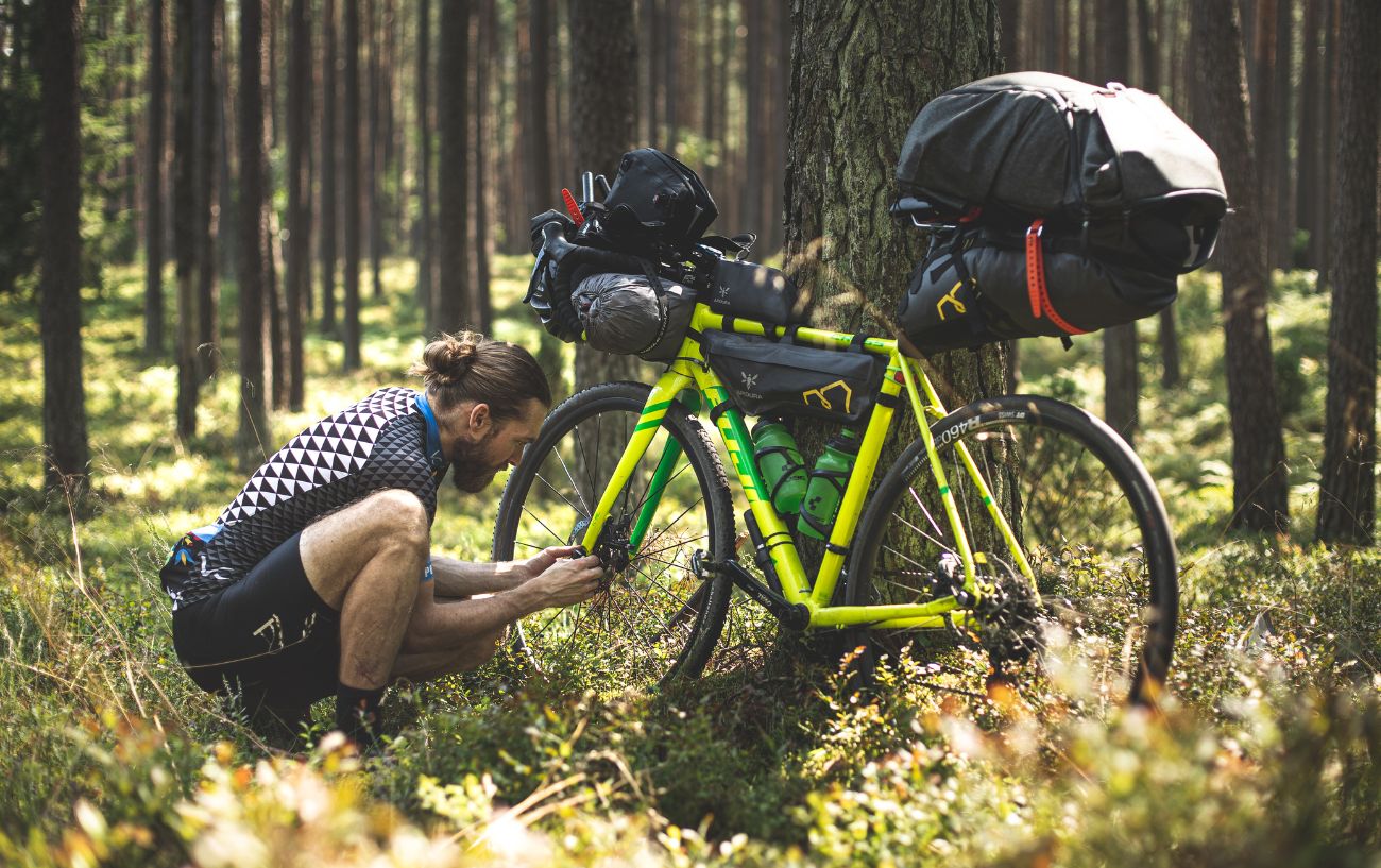 A bikepacker adjusts his bike in a forest.