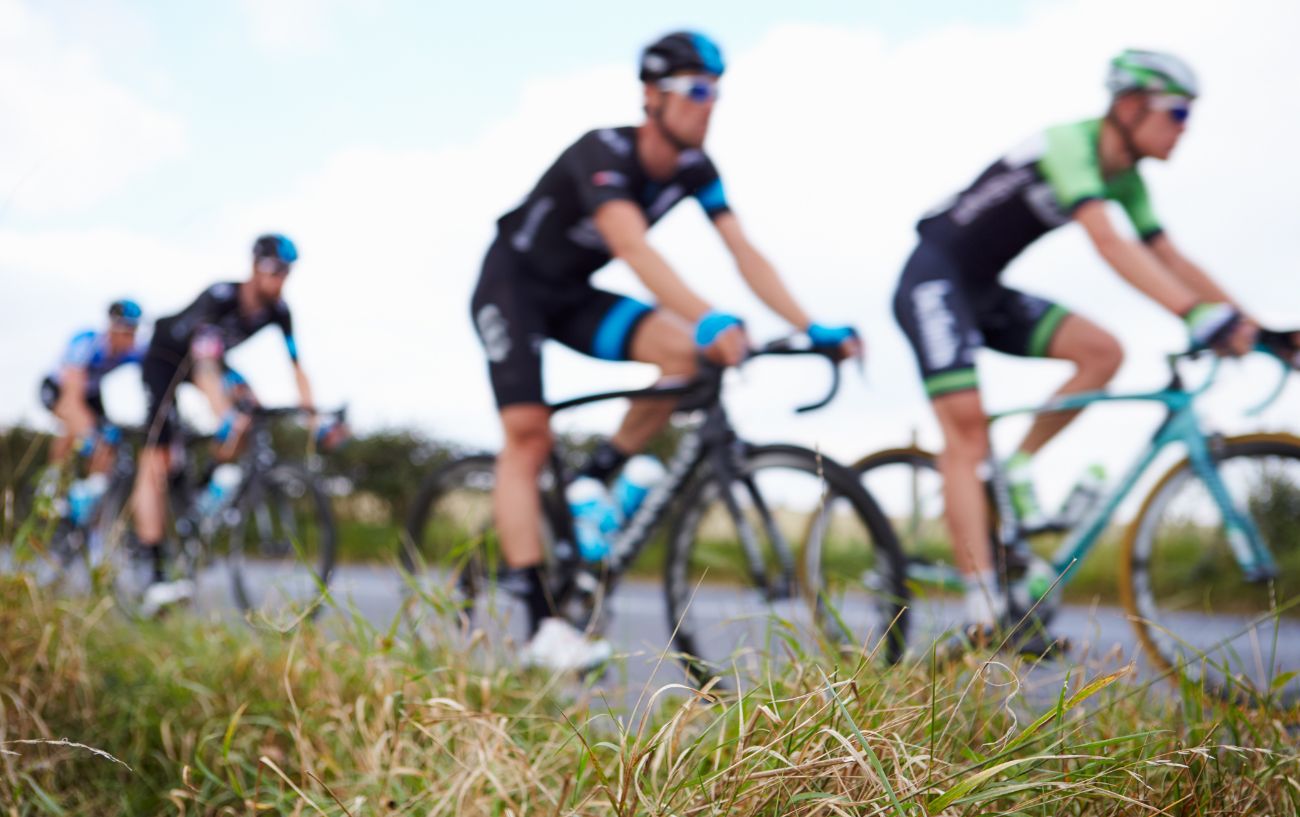 A group of pro cyclists ride past a grassy verge.