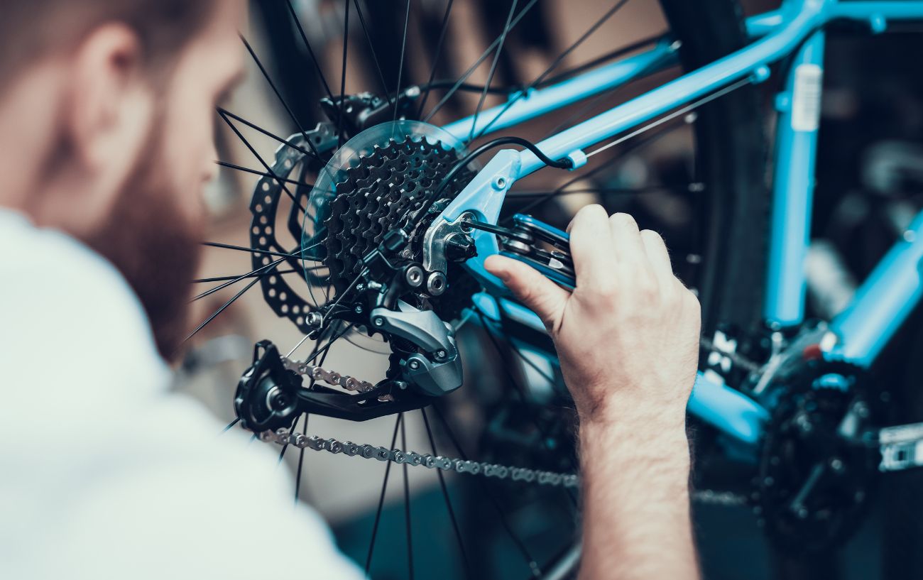 A mechanic uses a bike tool on the rear wheel of a blue mountain bike.