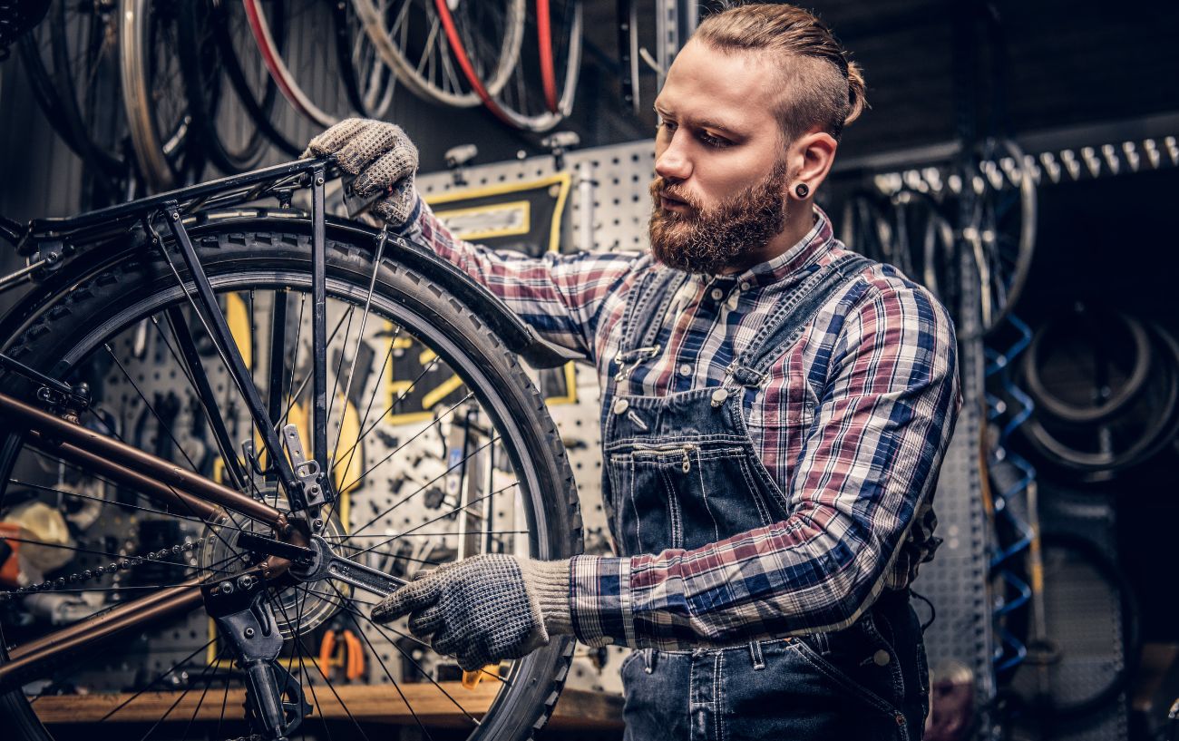 A bike mechanic uses a spanner on the rear wheel of a brown hybrid bike.