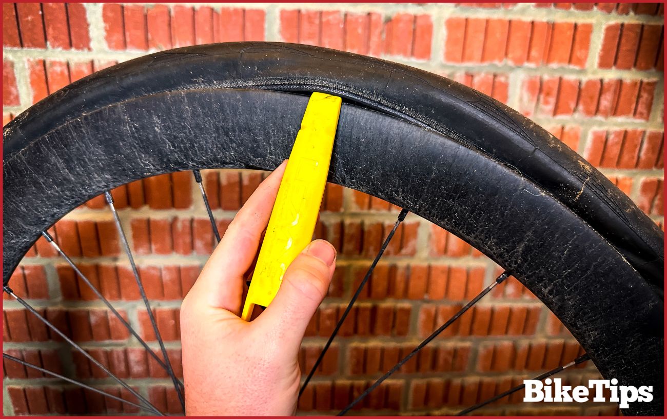 A yellow plastic tire lever unhooks the tire from a bike wheel's rim.