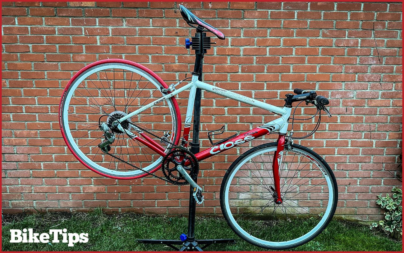 A hybrid bike is held up in a bike maintenance stand against a brick wall.