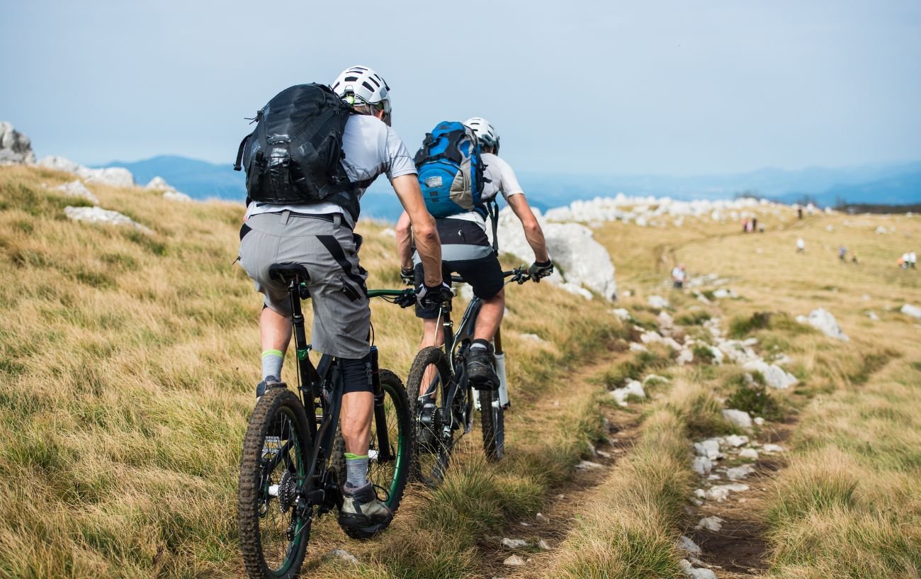 Two cyclists cruise along a rocky hilltop trail on mountain bikes.