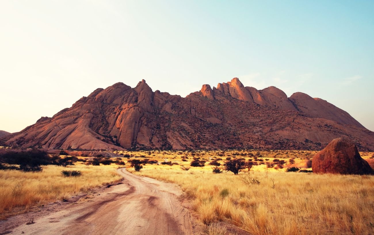 A dirt road leading to a rock formation in Namibia.