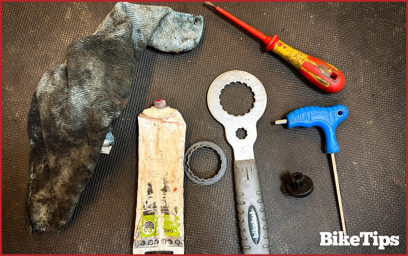 The tools you'll need to remove a bottom bracket lie on a black rubber work surface.
