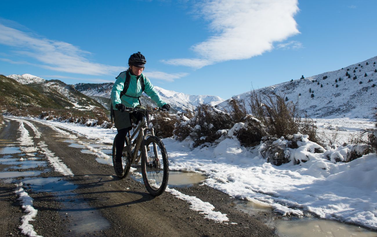 A cyclist rides along a snow-covered mountain road on a mountain bike.