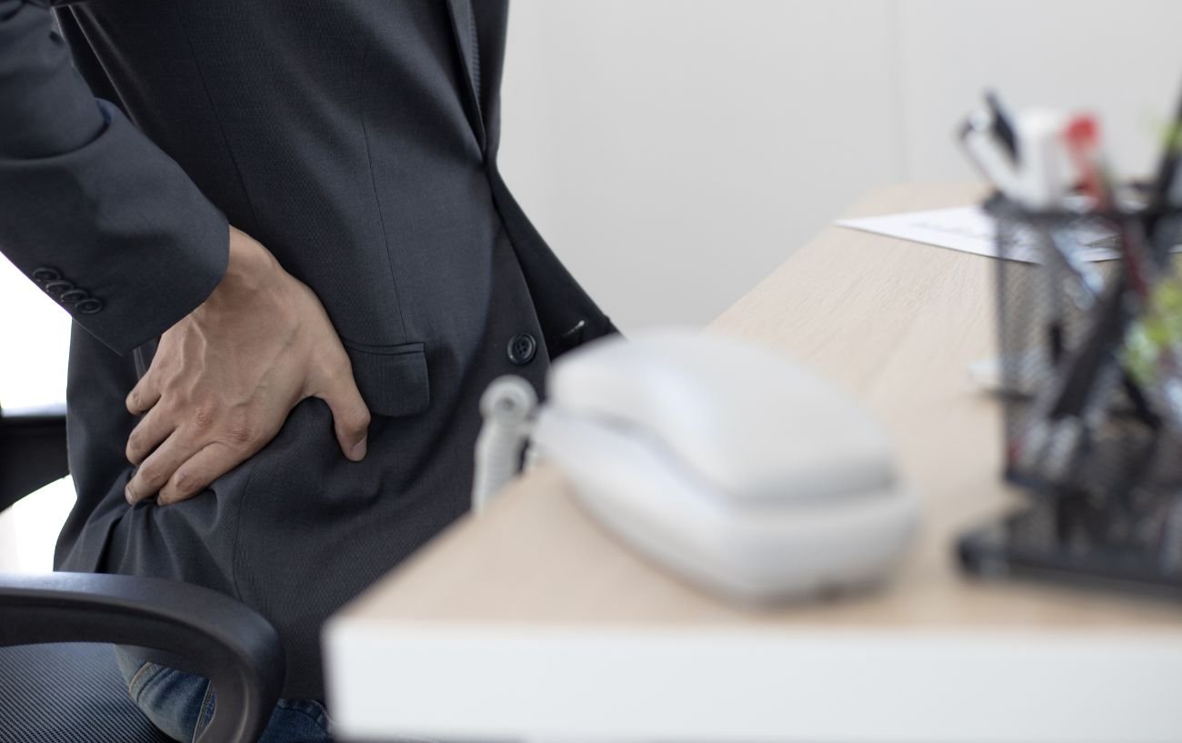 A worker in a suit suffers from hip pain at his desk.