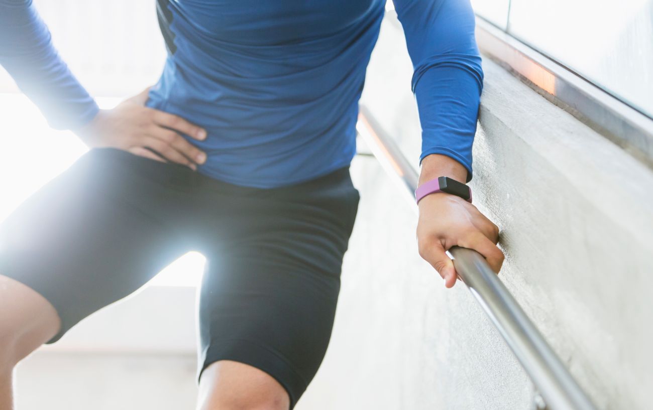 A cyclist in a blue shirt hold his hip in pain while descending stairs.