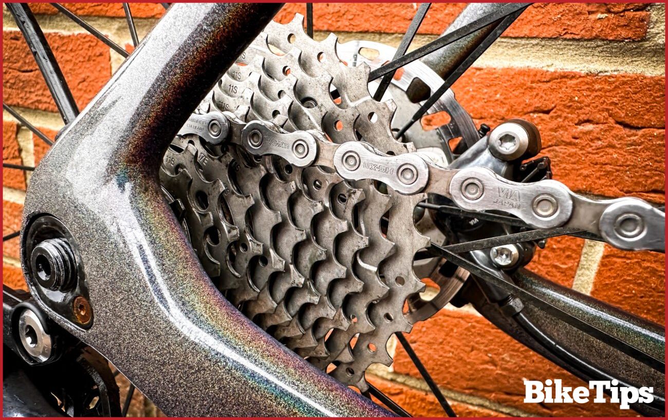 Close-up of a clean bike chain and rear hub against a brick wall.