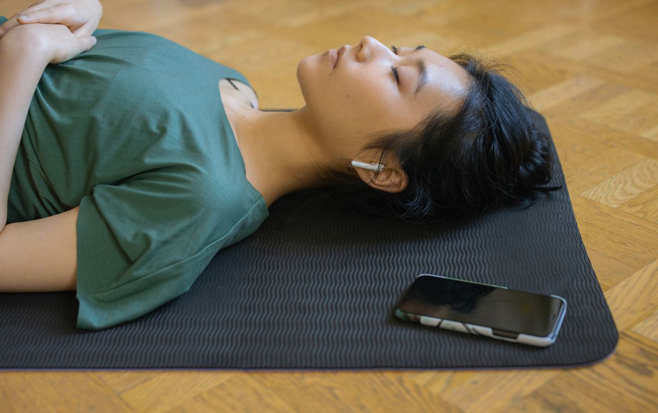 A cyclist rests on a yoga mat with her AirPods in after a Peloton workout.