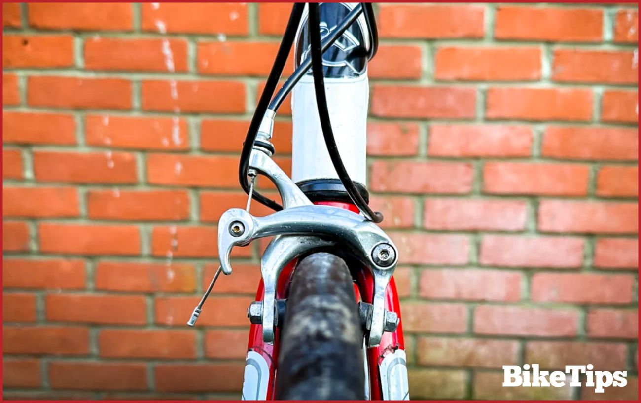 Close-up of dual-pivot caliper rim brakes on a white hybrid bike.