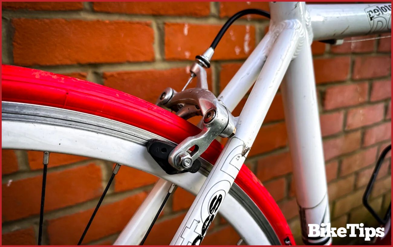 A silver rim brake on a wheel with a red tire.