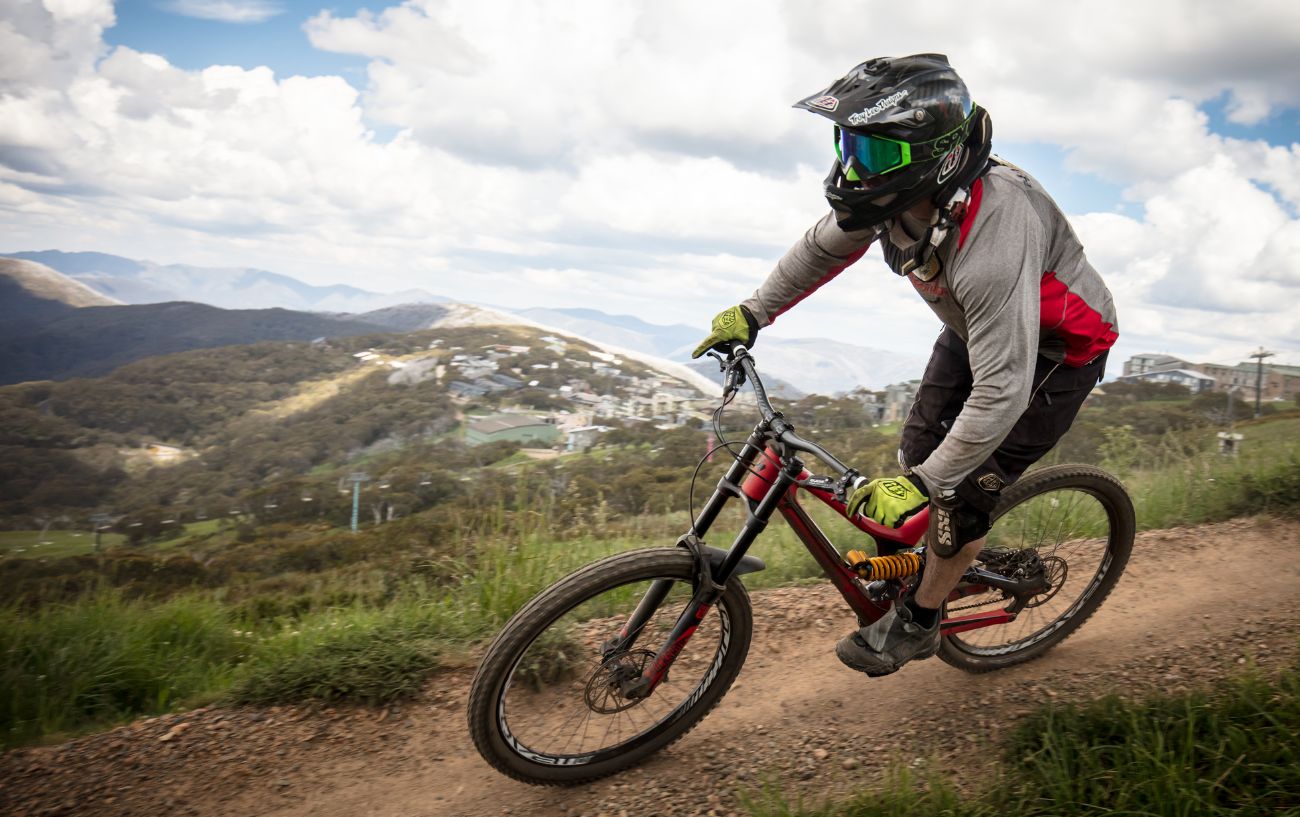 A mountain biker rides a downhill bike with wide handlebars.