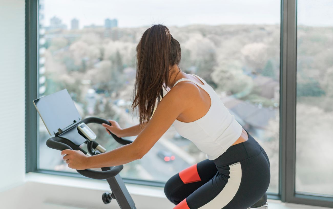 A cyclist rides her Peloton bike in a whitewashed apartment.