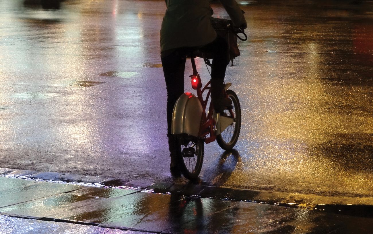 A cyclist rides a folding bike through a rainy city at night.