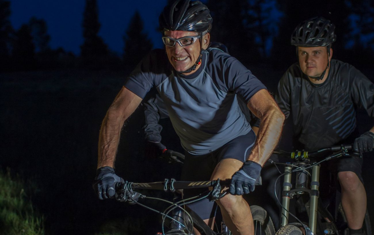 A pair of cyclists ride a mountain bike trail at night.