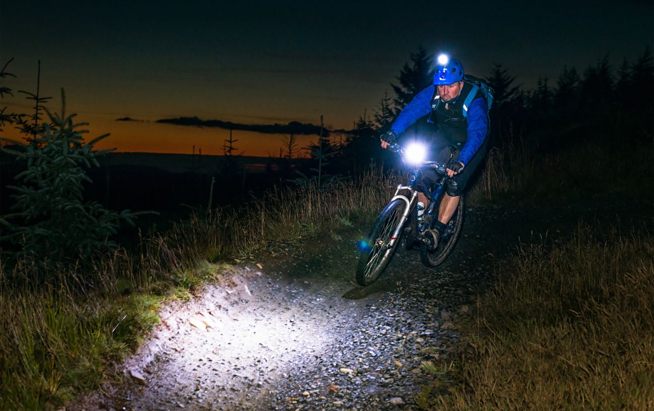 A cyclist rides along a gravel path at night.