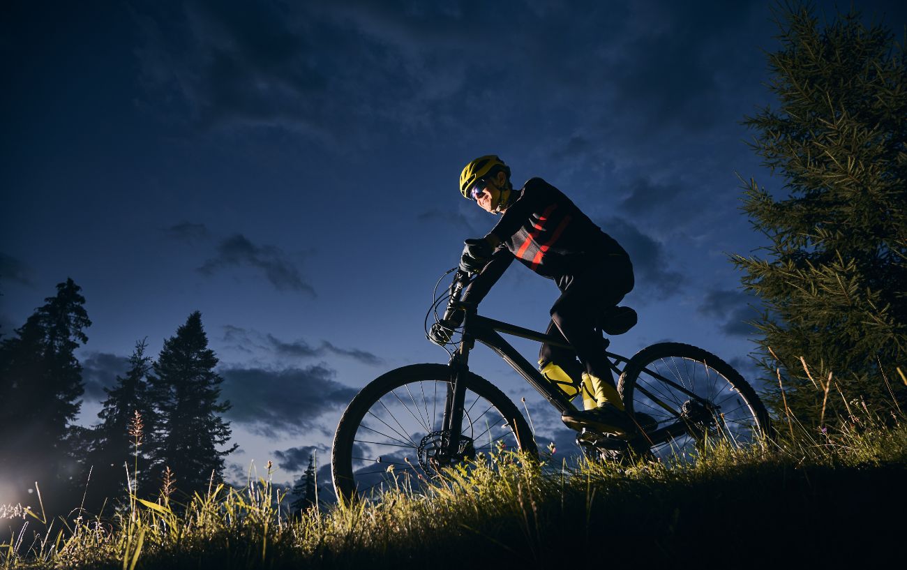 A mountain biker descends a grassy hill at night.