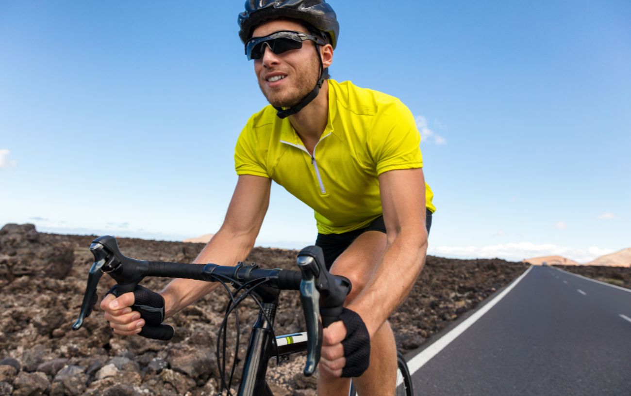 A cyclist in a green jersey rides a black bike fitted with grey brifters.
