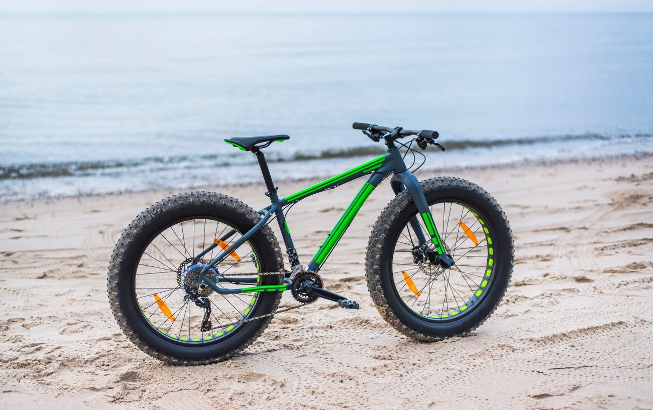 A green fat bike sits on a sandy beach.