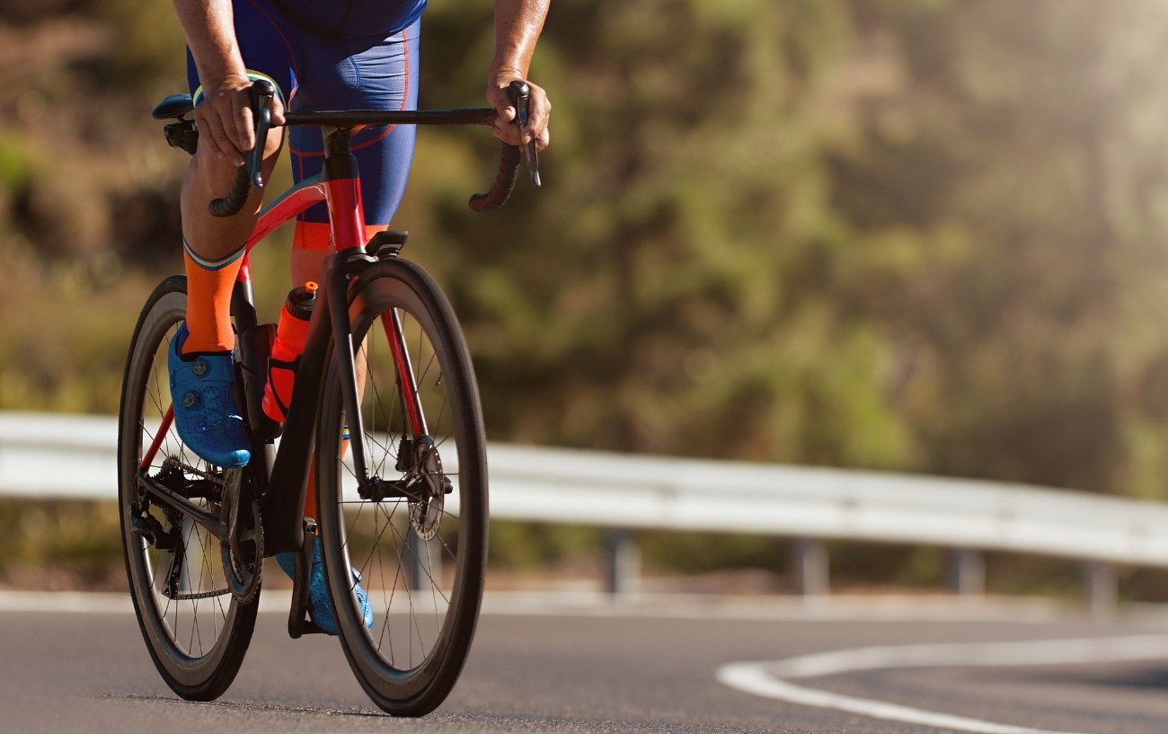 A cyclist on an orange road bike climbs on an asphalt road.