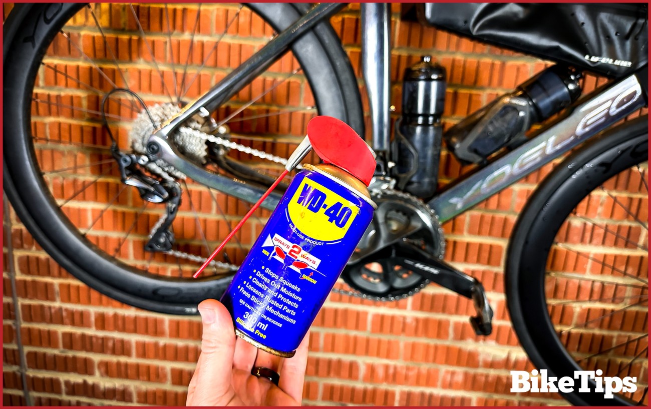 A can of WD40 is held in front of a black road bike.