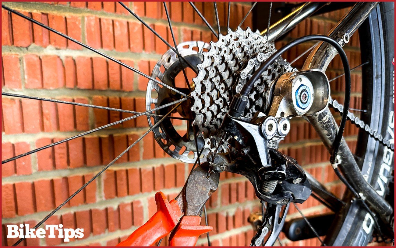 Using cable cutters to trim the excess cable from the back of a rear derailleur.