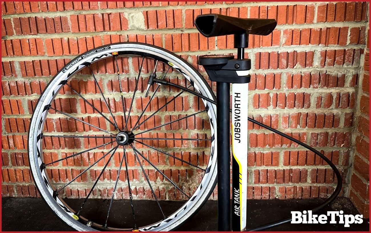 A bike pump and bike wheel lean against a brick wall.