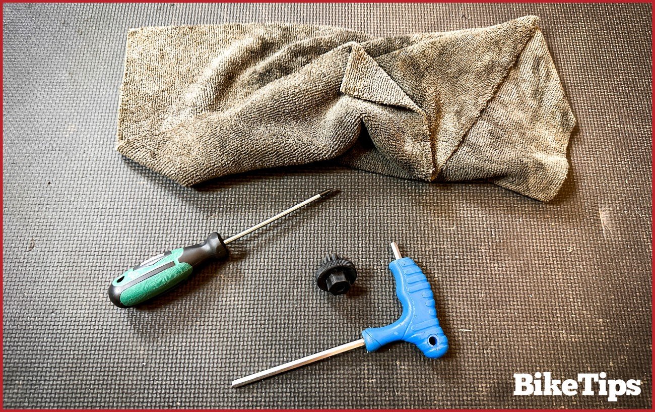 A screwdriver, Allen ket, and rag sit on a black floor.